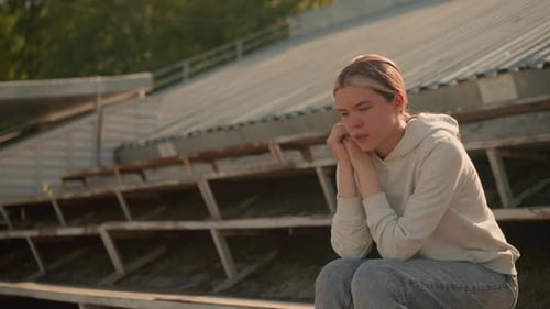 Pensive Woman in Hoodie Sitting on Rustic Stadium Bleachers