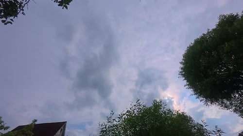Zeitraffer der Sonne, die am blauen bewölkten Himmel untergeht, mit Baum und Haus im Vordergrund