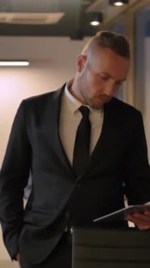 Vertical of Young Man Looking at Tablet PC at Evening Business Centre