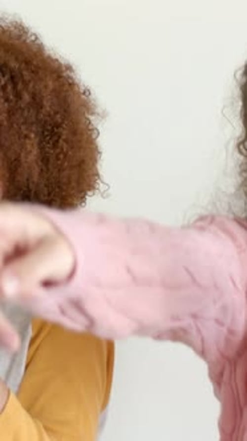 Vidéo verticale : micro levé, femme à gauche chantant en duo dans une pièce lumineuse, amie en pull rose pointant