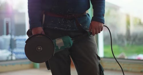 Worker holding angle grinder, ready for construction task, close-up of tool and worker’s hands