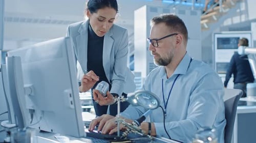Una ingeniera industrial habla con un especialista en electrónica, sostiene un prototipo de componentes metálicos,