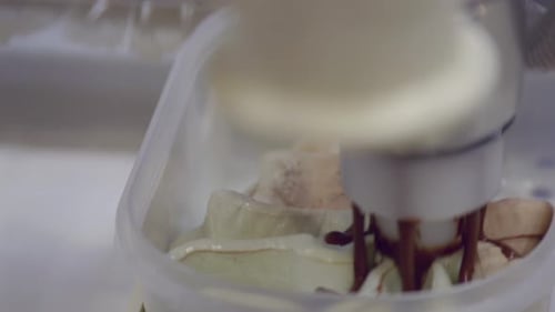 Close shot of a mechanical arm filling the freshly made ice-cream in a pattern in squround container