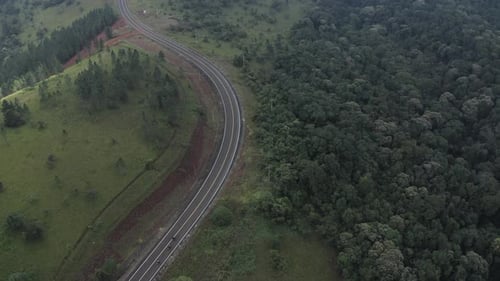4k POV Aerial shot over a hill top road surrounding by a beautiful green forest