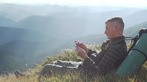 A Man with a Backpack Takes Pictures of Mountain Nature on His Phone