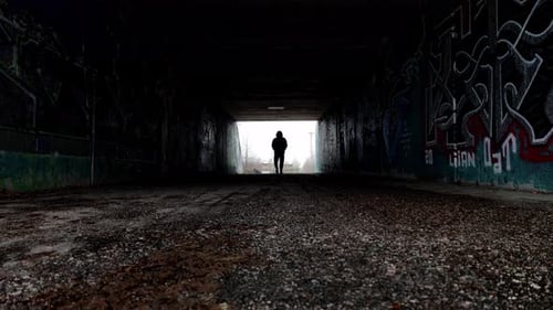 Silhouette of a man walking in dark tunnel towards the camera. Slow motion movement. Depression and