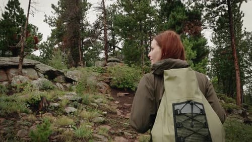 A girl backpacker hikes through a green forest. She looks over and smiles.