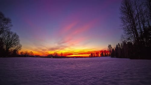 Farbenfroher Sonnenaufgang an einem teilweise bewölkten Morgen über einer schneebedeckten Wiese. Zeitraffer