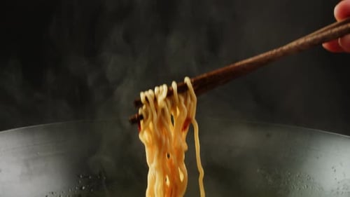 Chopsticks Holding Noodles above Steaming Wok