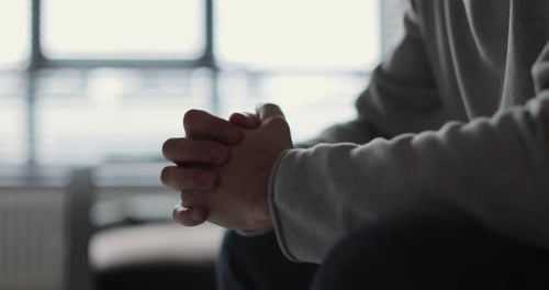 Person Sits With Clasped Hands in Indoor Setting