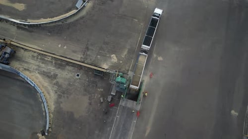 Worker in industrial factory working with Grain cargo truck at unloading process. Aerial top down.