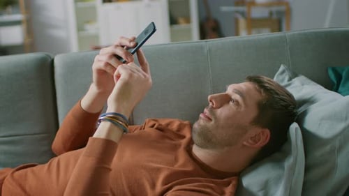 Relaxed Man Using Smartphone on Couch at Home