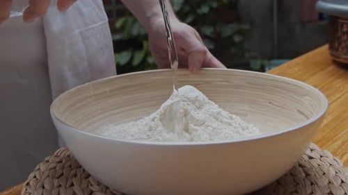 Der Koch gießt Wasser auf den Pizzateig in einem tiefen Teller. Rezept für die Zubereitung von Pizza. Zeitlupe.