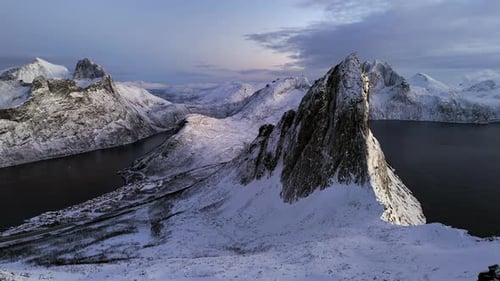 Cinematic aerial view of Segla peak on Senja Island, Norway, steep snow-covered cliffs above icy