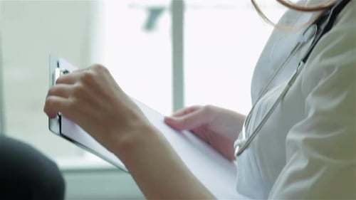 Woman Doctor Writes on Clipboard in Office