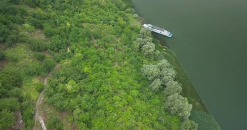 a slope that leads to the river filled with green trees towards the ship moored to the shore