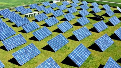 A solar farm with rows of blue solar panels on green grass, aerial view