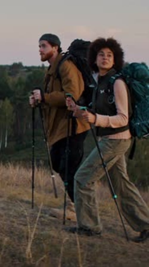 Young Man and Woman Hikers Walk Uphill Using Nordic Walking Poles