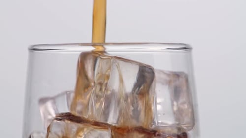 Close Up Of Fresh Cola Being Poured In To The Glass With Ice Cubes On White Background