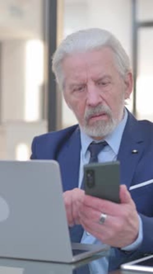 Senior Man Using Phone and Laptop Indoors