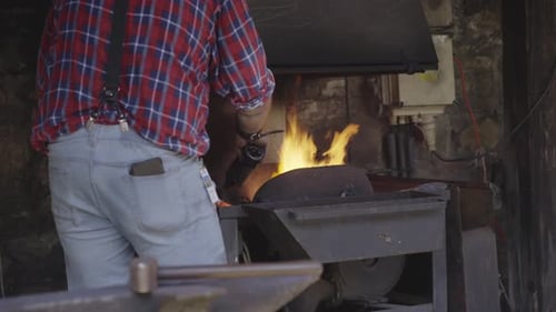 Schmied, der mit einer Schmiede arbeitet und Flammen erzeugt, während er an der Metallbearbeitung arbeitet.