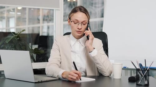 Businesswoman on Phone Taking Notes in Office