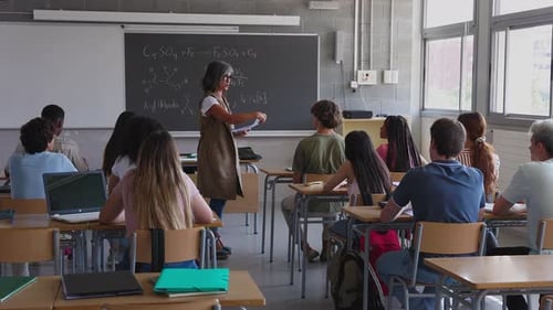 High School Teacher Handing Out Tests to Her Students in Classroom