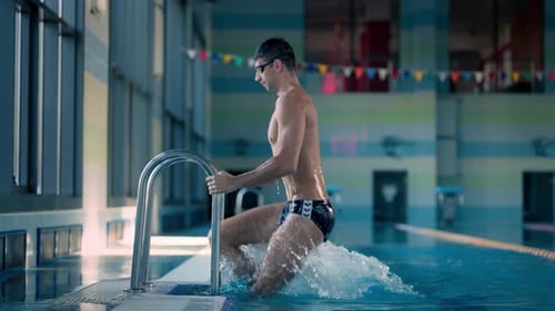 Un hombre atlético sube una escalera de metal en una piscina pública durante el entrenamiento