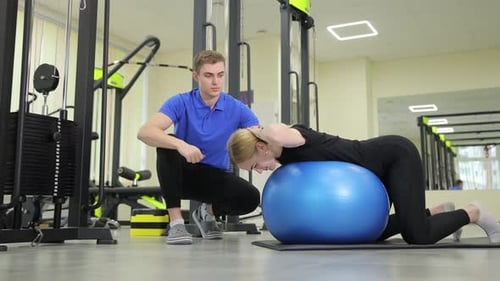 Woman Using Exercise Ball with Trainer in Gym