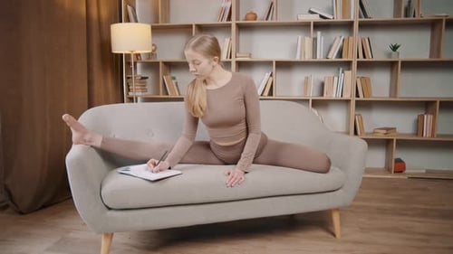 Woman in Splits on Sofa Writing in Notebook