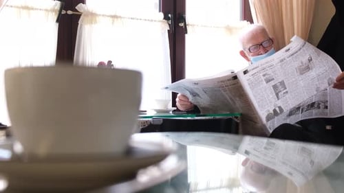 Senior Adult Reading Newspaper with Coffee Indoors