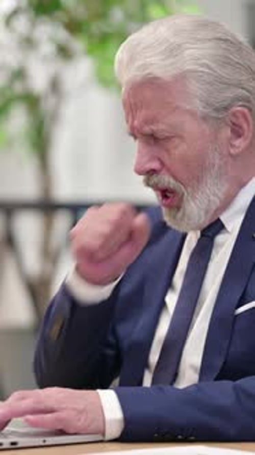 Senior Man Coughing While Working at Laptop