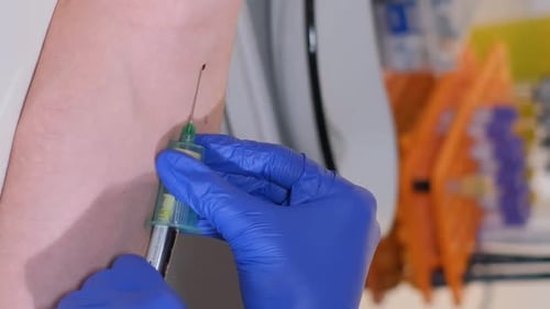 Eine Krankenschwester in Handschuhen entnimmt Blut aus der Vene eines Patienten und führt eine Punktion mit einer Nadel durch. Vertikales Video
