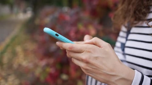 Closeup of a Young Woman's Hands Using a Modern Smartphone in a Picturesque Autumn Park Surrounded