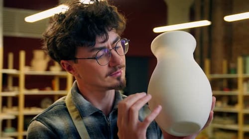 Young Man Inspecting Pottery Vase in Workshop
