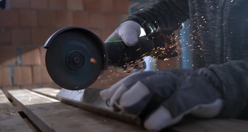 Angle grinder cutting metal with sparks flying, craftsman’s gloved hands holding metal in place