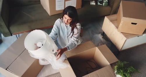 Woman unpacking lamp sitting amongst moving boxes