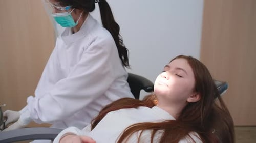Dentist woman use tools to shine blue light into oral cavity of young girl children during treatment