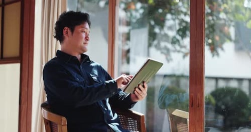 Man Sitting in Chair, Looking at Tablet