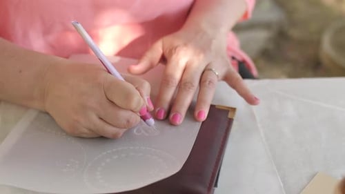 caucasian woman in pink dress embossing parchment craft in garden, closeup pan