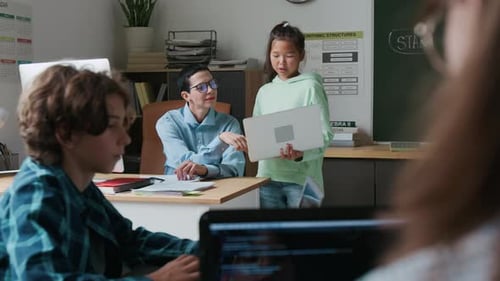 Teacher Works With Students in Classroom on Laptops
