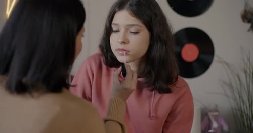 Mutter und Tochter tragen Lipgloss auf, schminken sich, lächeln, binden, im Schlafzimmer zu Hause