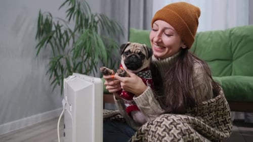 Woman and Dog Warming Up by Heater Indoors