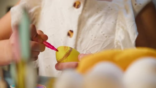Une petite fille peint des œufs de Pâques avec un stylo-feutre en gros plan