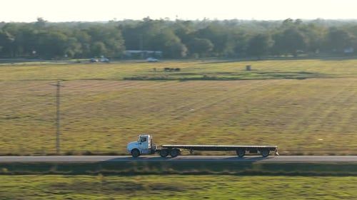 Two Lane Road Through Open Fields with Flatbed Truck Tractor Trailer Moving Forward at Golden Hour