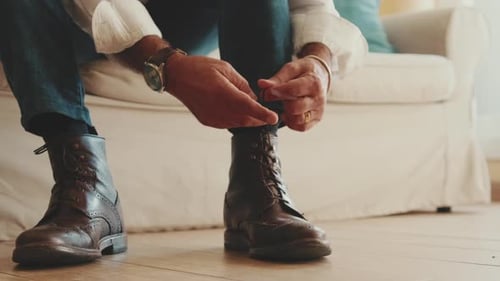 Close-up of legs of man putting on casual boots, tying shoelaces