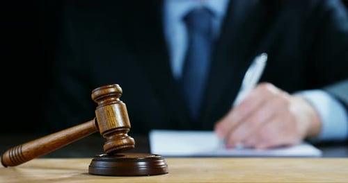 Gavel On Desk Near Blurred Person Writing