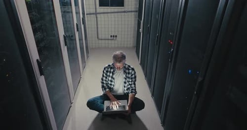 Man with Laptop in Dark Server Room
