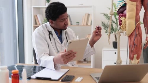 Doctor Consults Tablet While Reviewing Medical Skeleton