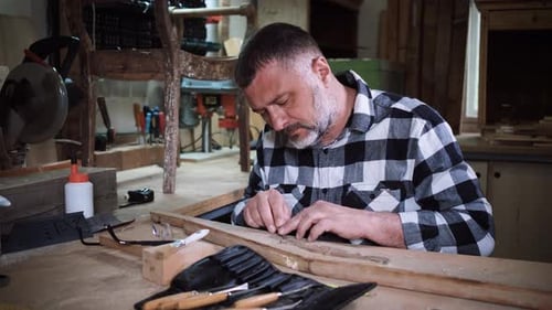 Carpenter sitting in his workshop restoring old piece of furniture with carving tool.